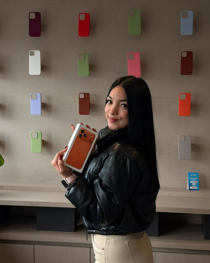 Clienta con la caja de su iPhone frente al muro de carcasas del showroom